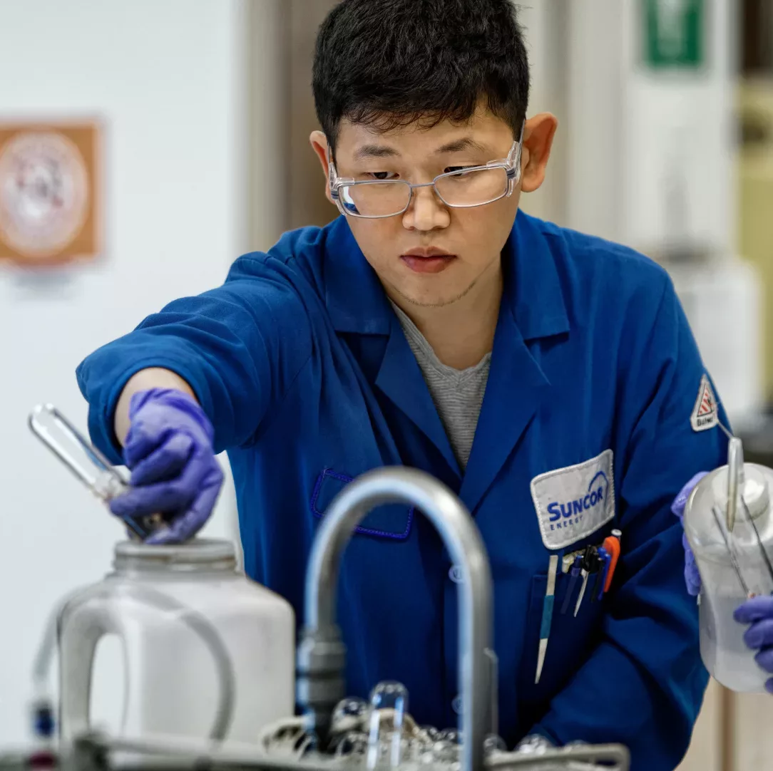 Une personne portant une blouse bleue, des lunettes de protection et des gants, travaillant dans un laboratoire de recherche et développement.
