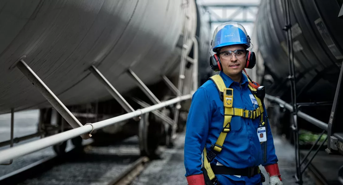 Un travailleur se tient debout parmi les équipements de l’installation; il porte un équipement de protection et sourit.
